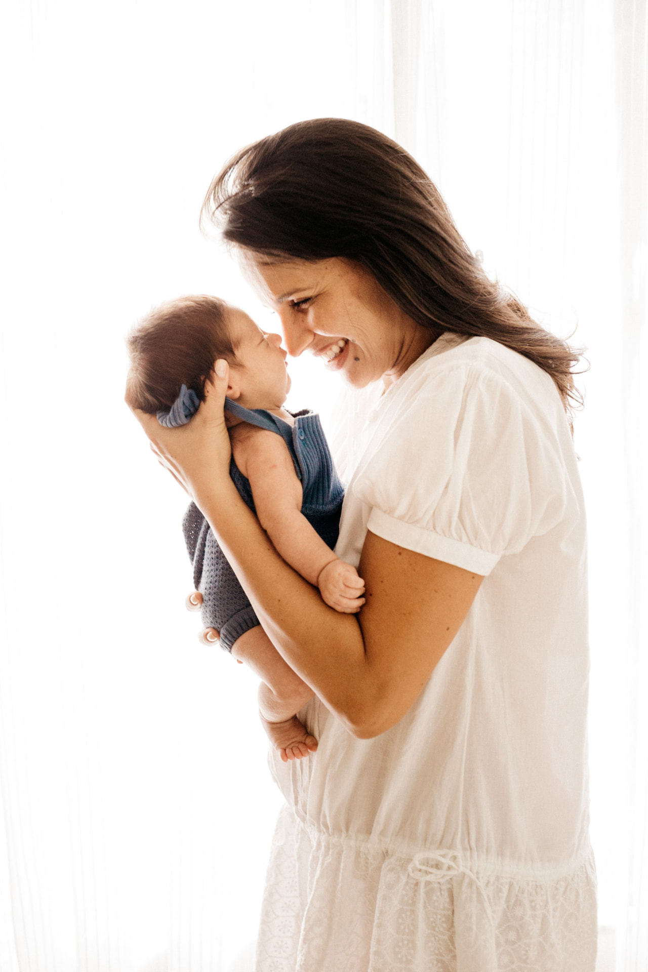 A mother smiling as she holds her baby close in soft natural light
